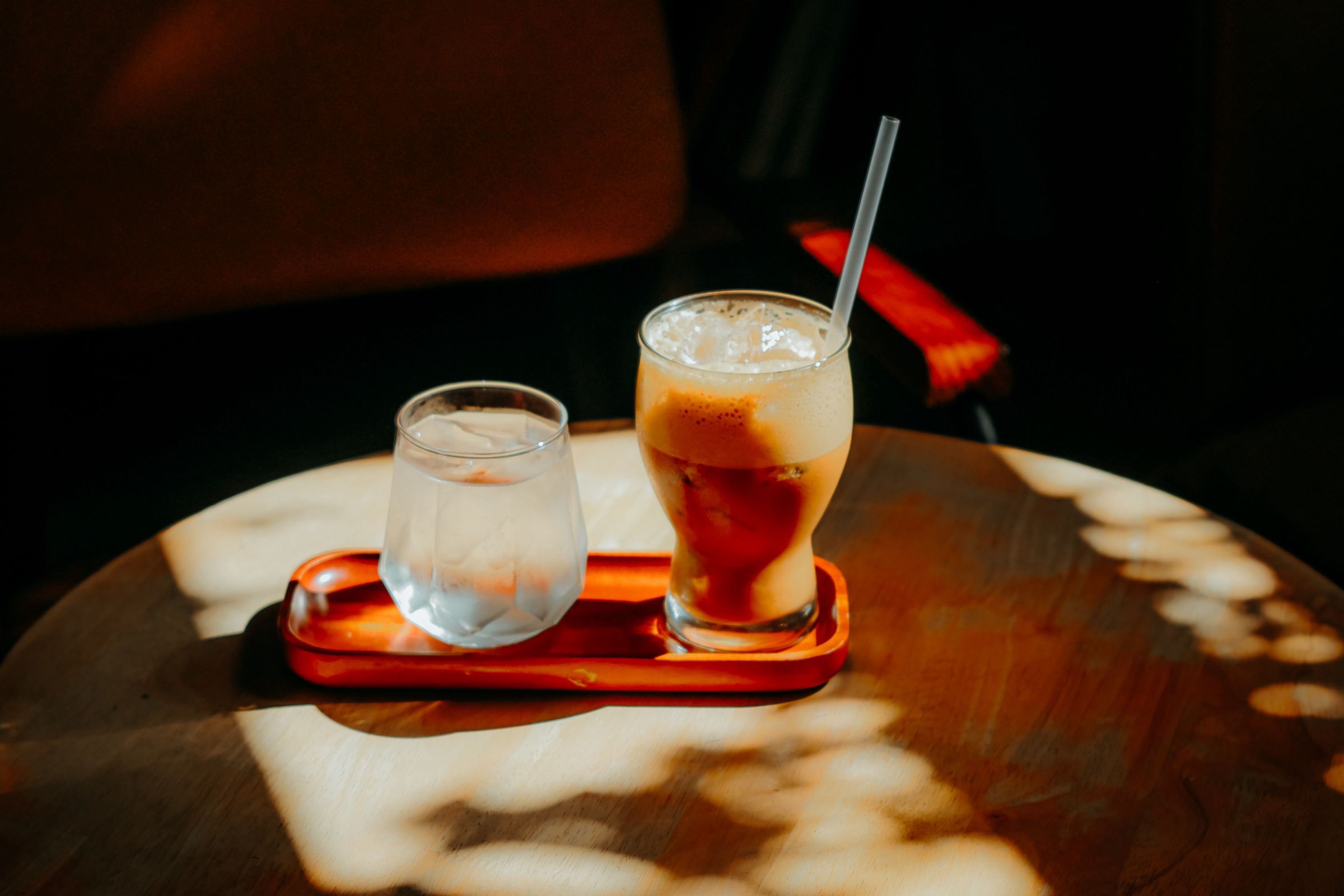 Ein Glas Eiskaffee und ein Glas Wasser auf einem Holztablett im Sonnenlicht