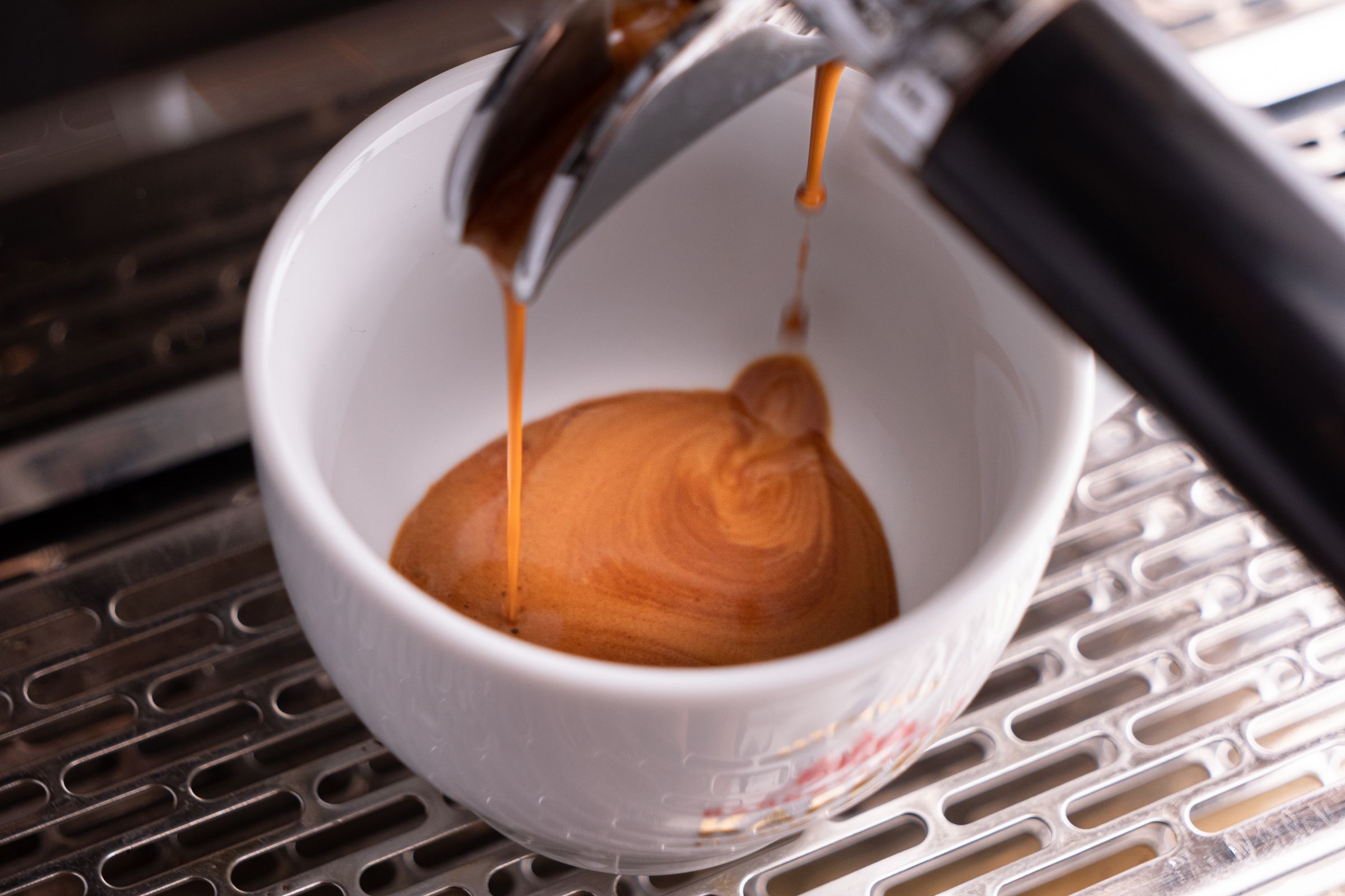 Espresso läuft aus dem Siebträger in eine weiße Tasse