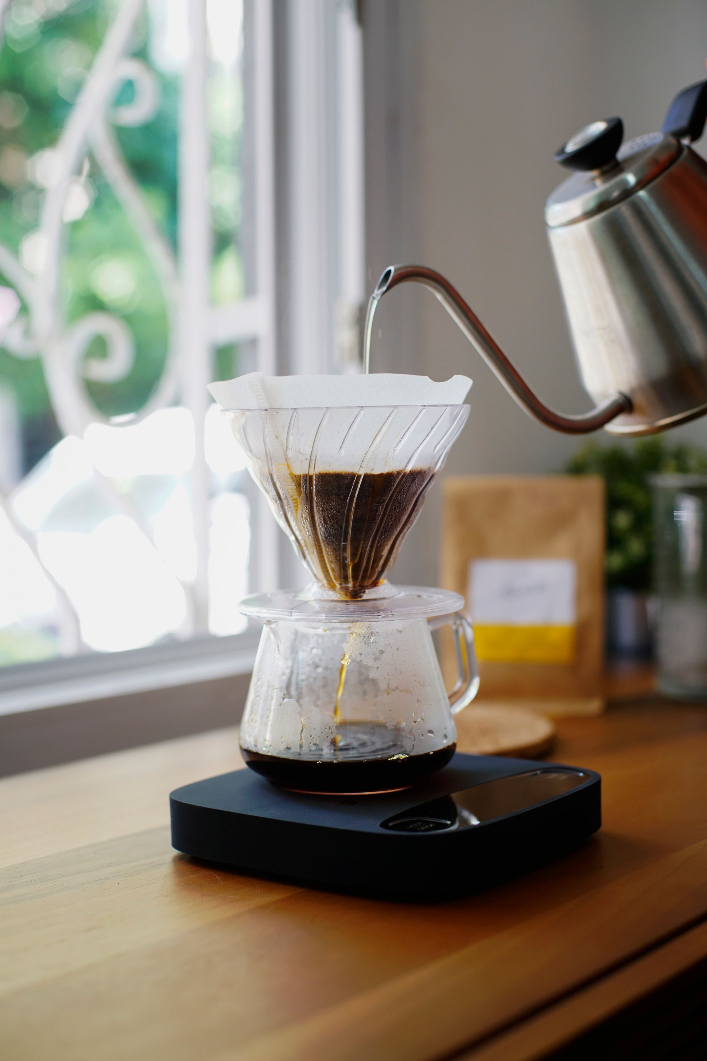 Handfilter mit Glaskanne am Fenster, Wasser wird aus einem Kessel aufgegossen